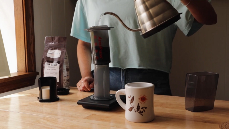 A person making coffee with an inverted Aeropress, pouring hot water over the grounds