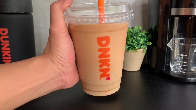 A homemade Dunkin’ Donuts Iced Coffee in a clear plastic cup with an orange straw and DNKN log