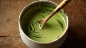 A bowl of freshly whisked matcha with a bamboo whisk, showing vibrant green tea and swirling patterns on a rustic wooden surface