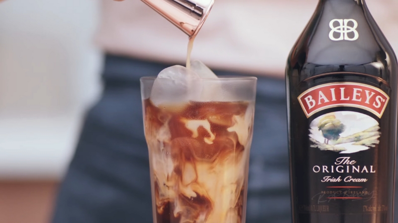Baileys poured into iced coffee in a tall glass beside a Baileys bottle