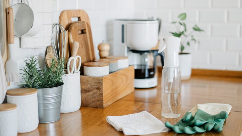 Neatly organized kitchen counter with wooden utensils, spice jars, coffee maker, and cleaning tools laid out